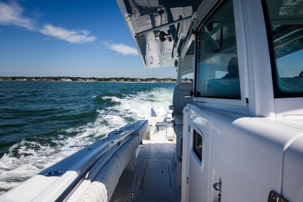 Side view of a white luxury boat cruising on blue water with a distant shoreline visible under a clear sky