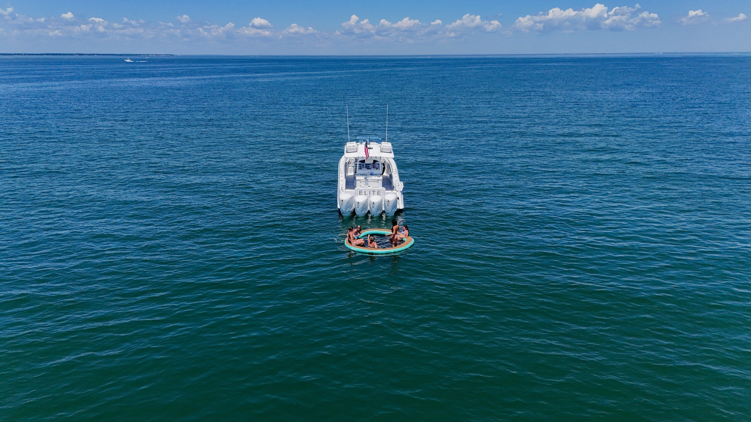 White motor yacht with a circular inflatable raft carrying people nearby on calm blue ocean