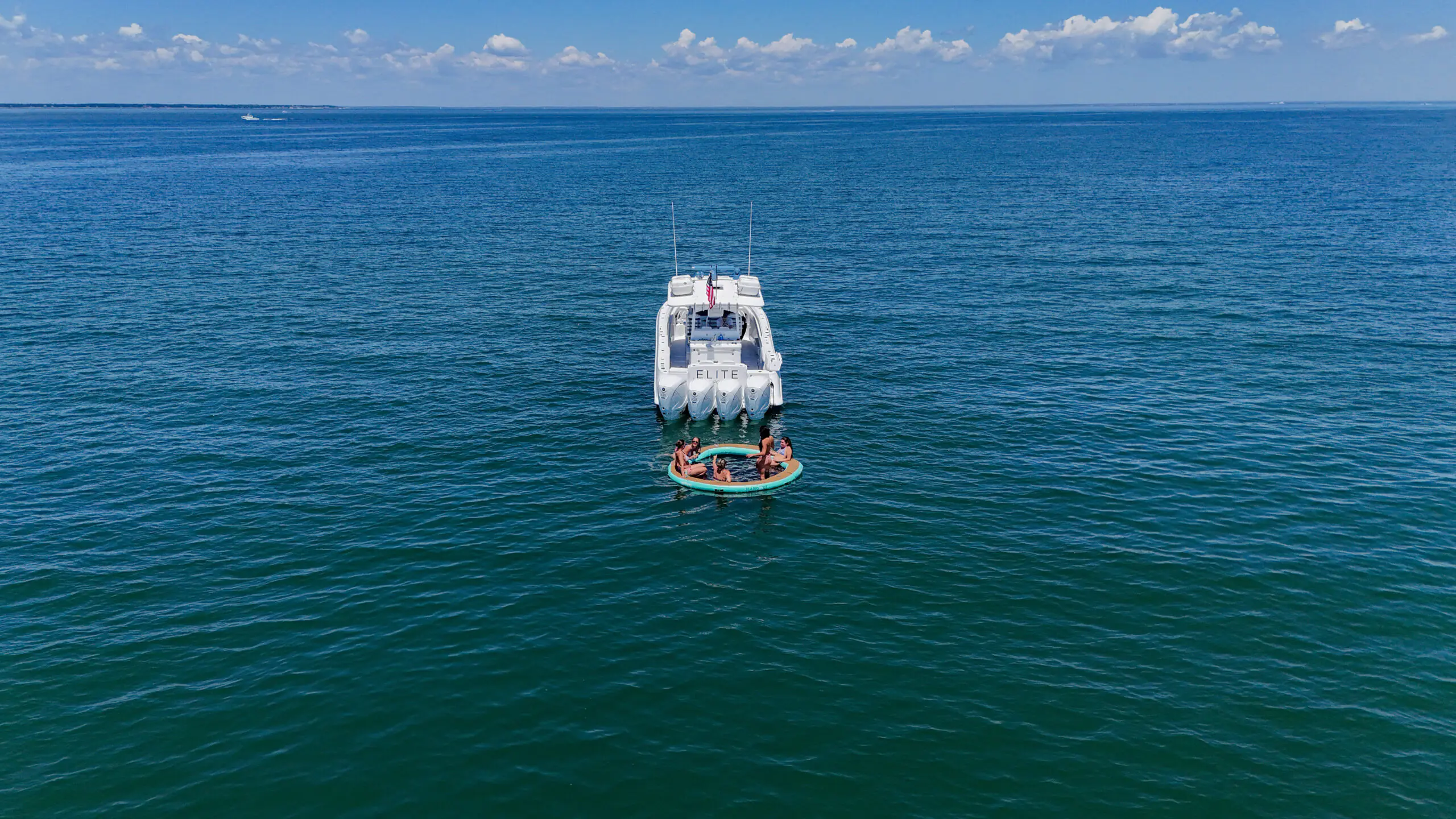 White motor yacht with a circular inflatable raft carrying people nearby on calm blue ocean